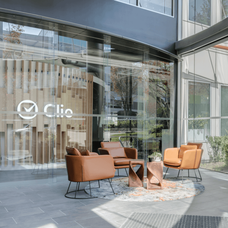 The glass entrance to the Clio headquarters in Burnaby, showing a modern lounge area with leather chairs inside.