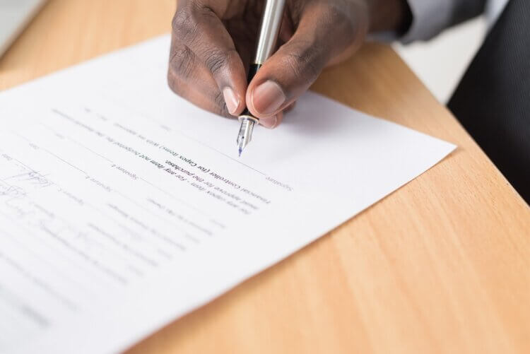 Person using a fountain pen to sign a contract with indemnity clauses.